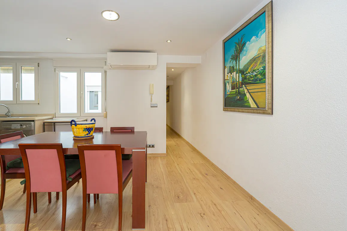 A bright dining area with a wooden table, pink chairs, and a painting of a tropical scene on the white wall.