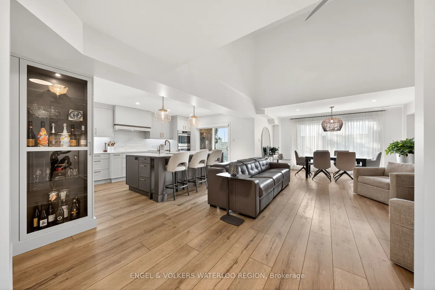 Open-concept living space with wood floors, featuring a kitchen with island, leather sofa, and dining area with a woven pendant light.
