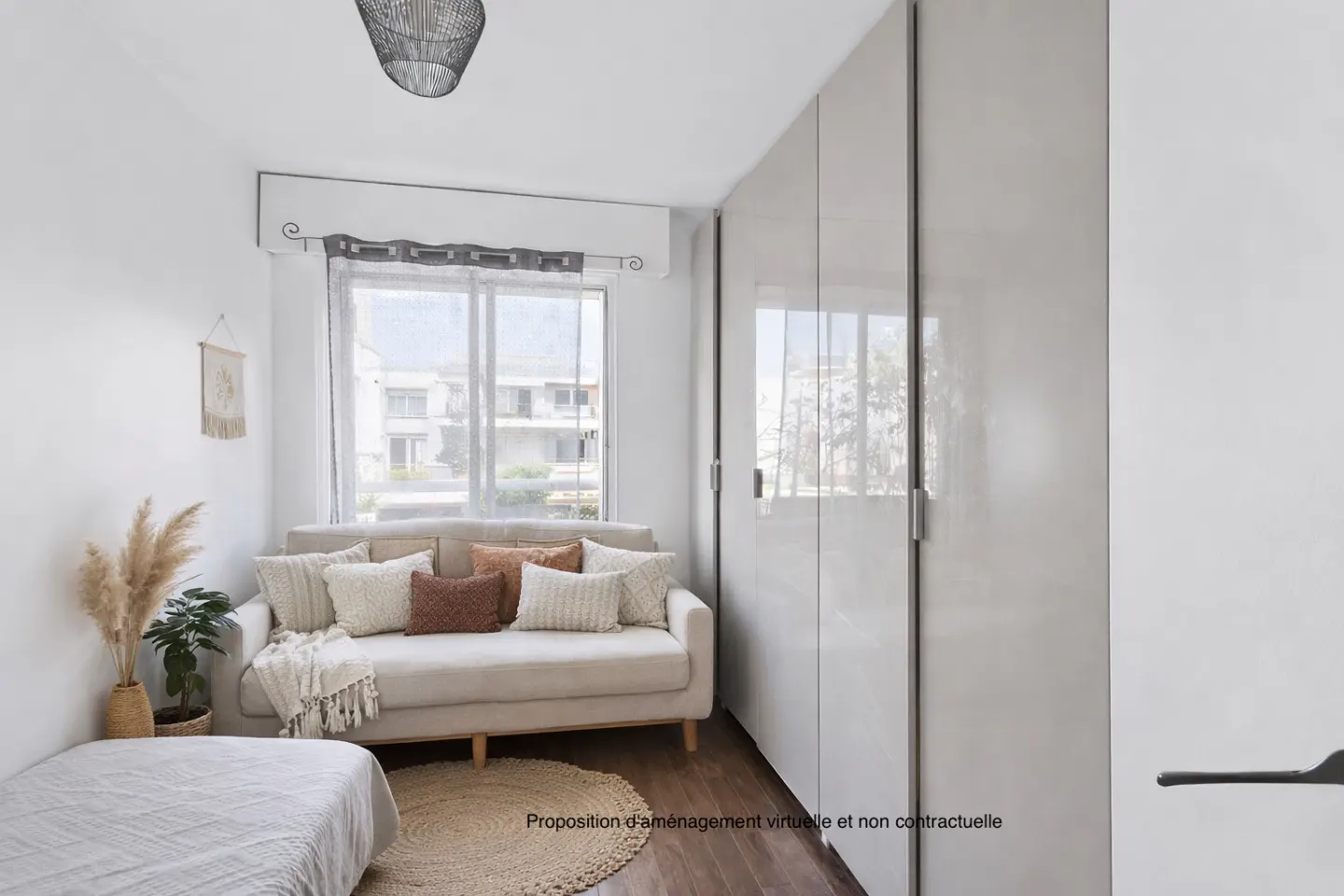 Bright room with a beige sofa, pillows, and a round rug. A large window with sheer curtains and a tall, glossy wardrobe are also visible.