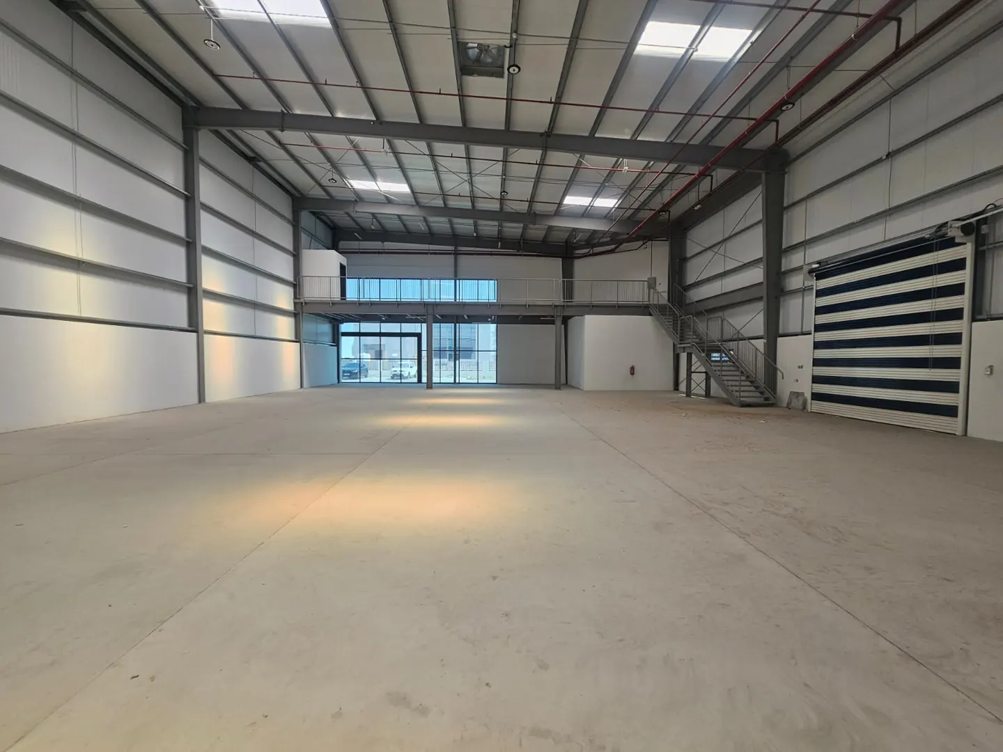 Interior of a large, empty warehouse with a concrete floor, metal beams, and a second-story office space.