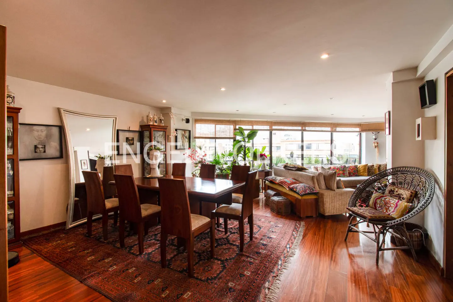Open-concept living and dining area with hardwood floors and a large oriental rug. A dining table with chairs sits near a wicker chair and sofa.