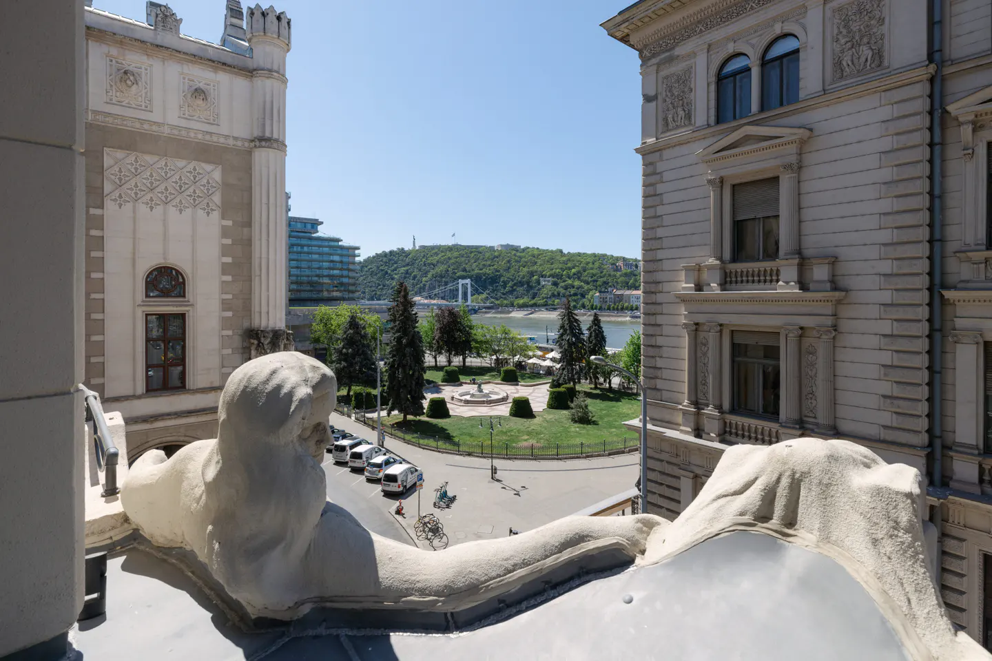 View from a building with stone statues overlooking a park, river, and bridge in the distance.
