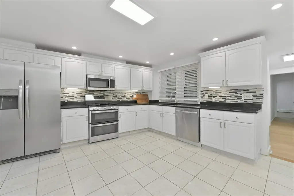 Bright kitchen with white cabinets, stainless steel appliances, and black countertops. Tiled floor and backsplash.