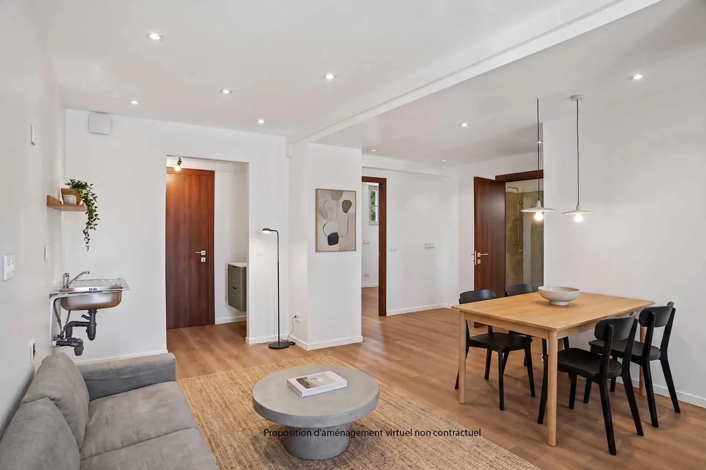 Bright apartment interior with a gray sofa, stainless steel sink, wood table with black chairs, and a round coffee table on a jute rug.