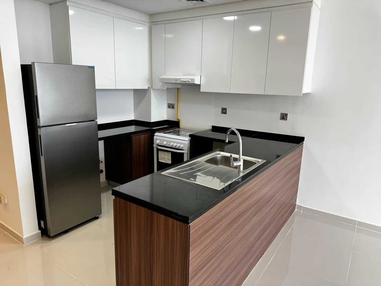 A modern kitchen with white cabinets, black countertops, and stainless steel appliances. A wood-paneled island features a sink and faucet.