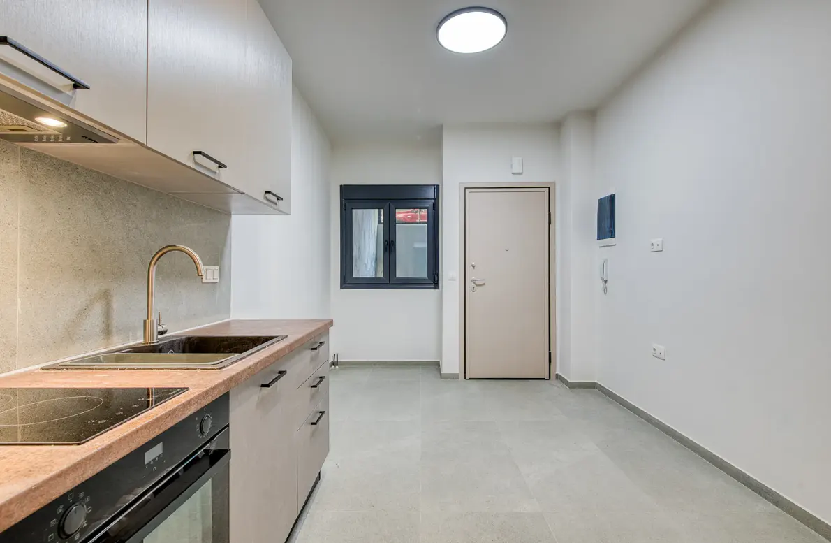 A modern kitchen with white walls, light gray cabinets, and a black cooktop. A window and door are visible in the background.