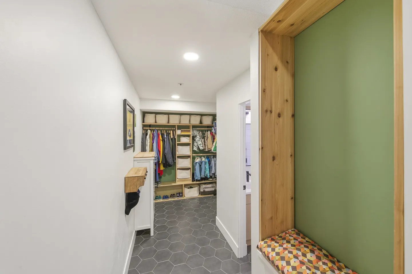 Hallway with a closet, a wooden bench with a patterned cushion, and gray hexagonal floor tiles.