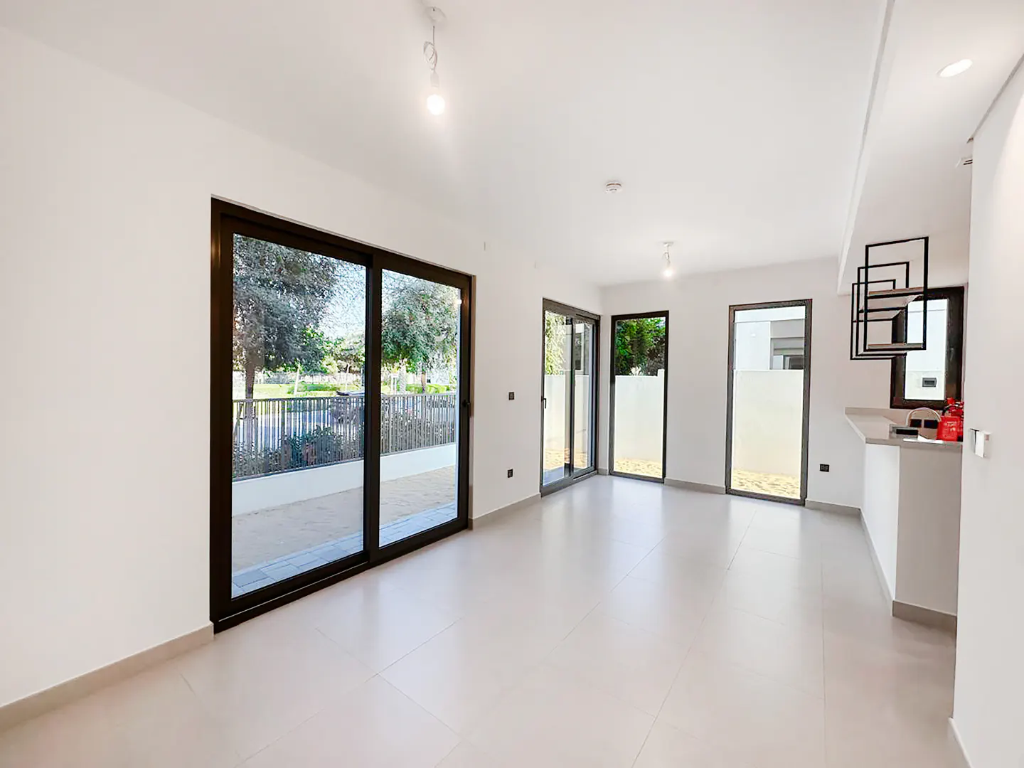 Bright, empty living room with white walls, light tile floors, and black framed sliding glass doors to a patio.