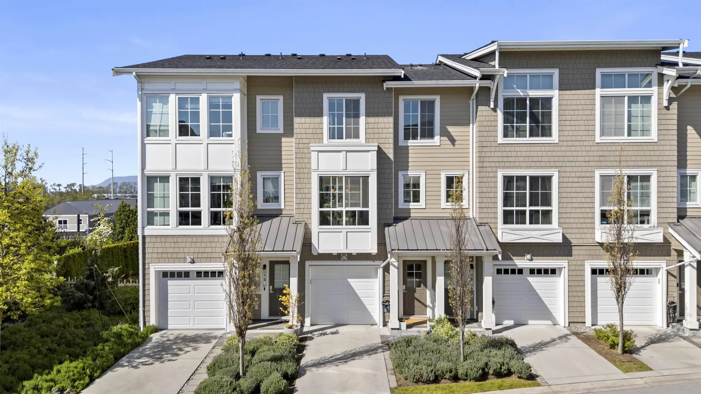 Three-story townhouses with beige siding, white trim, and white garage doors on a sunny day.