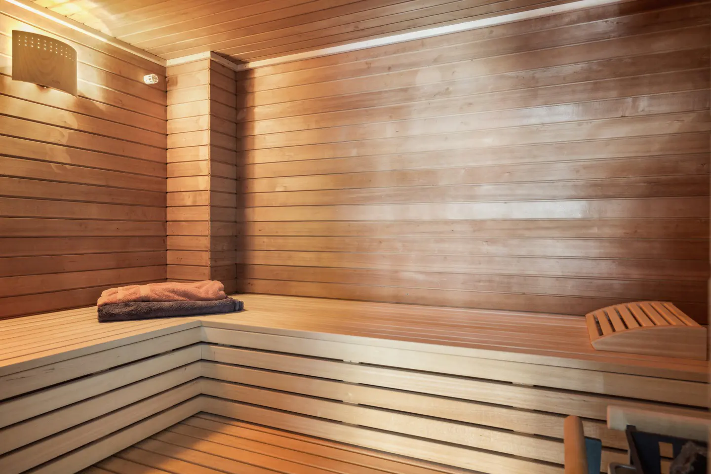 A sauna room with wooden walls, benches, towels, and a headrest.