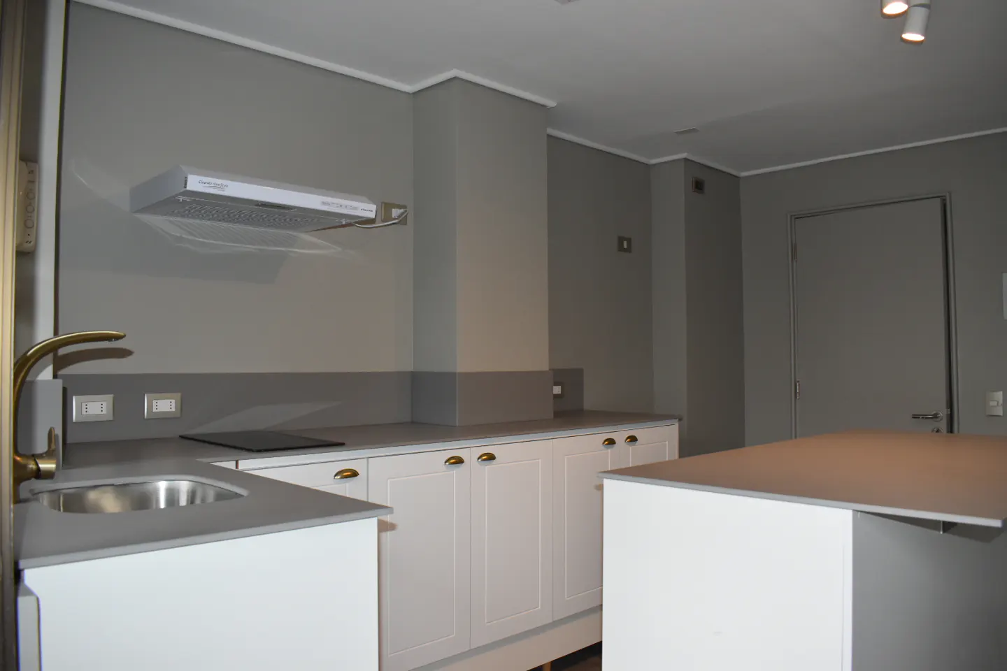 A modern kitchen with gray walls, white cabinets, and a gray countertop. A gold faucet is visible near a stainless steel sink.