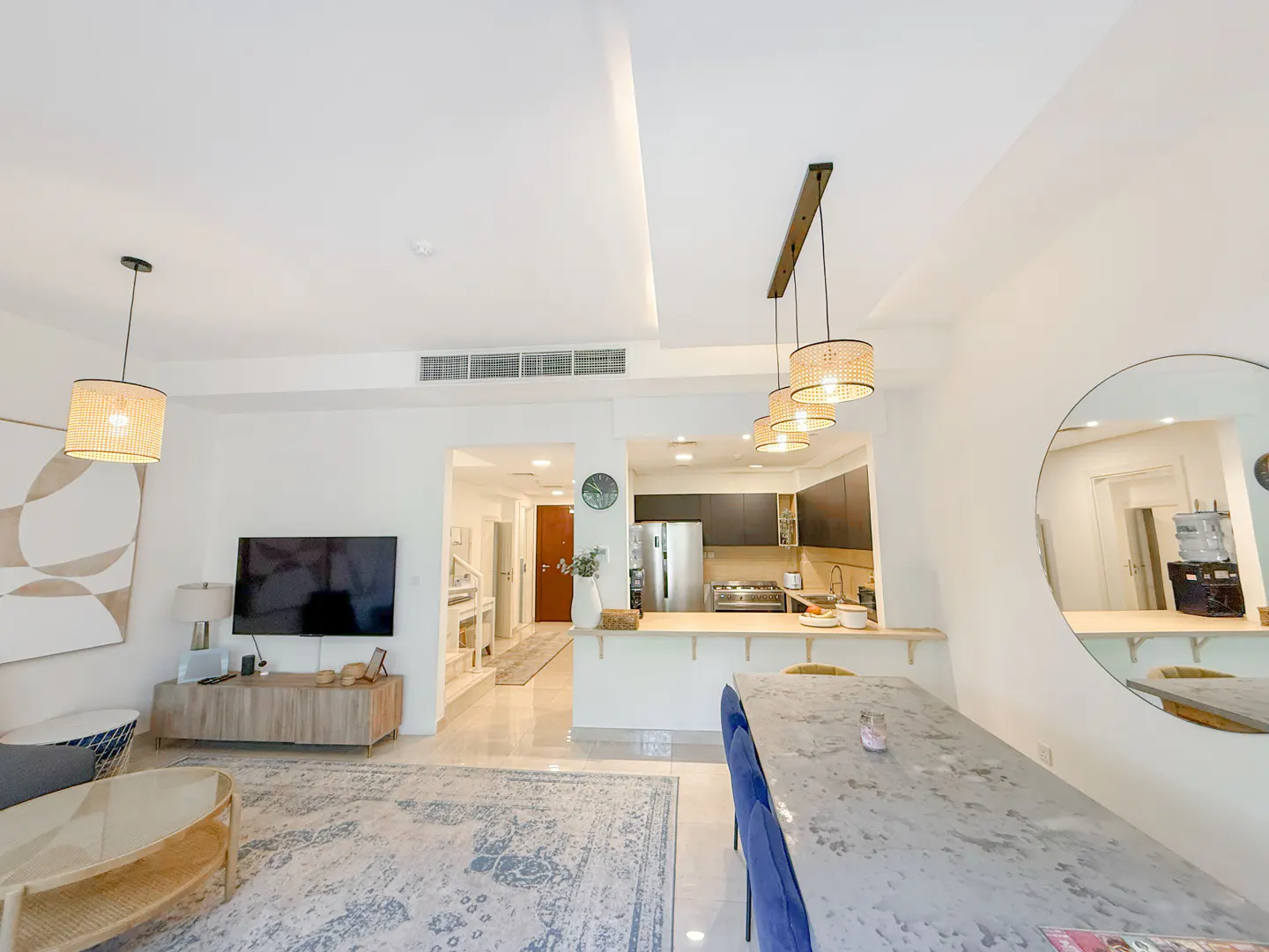 Open-concept living space with white walls, a dining table with blue chairs, and a kitchen with stainless steel appliances.