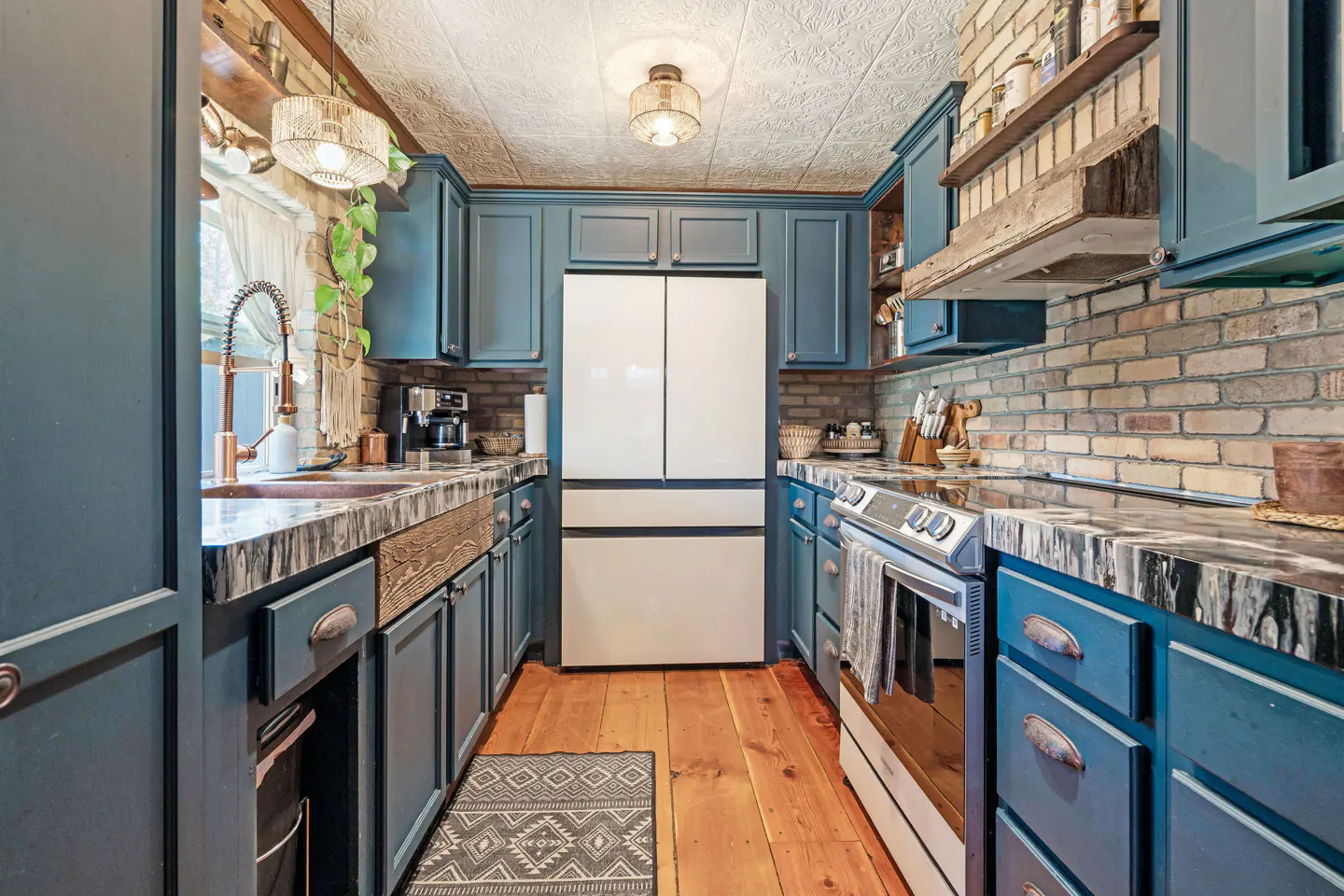 A kitchen with blue cabinets, brick backsplash, wood floors, and a white refrigerator.