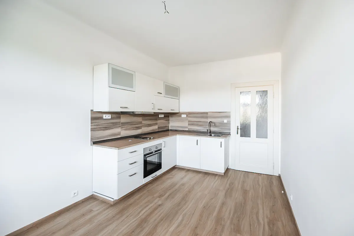 Modern kitchen with white cabinets, wood-look countertops, a built-in oven, and light wood flooring in a bright room.