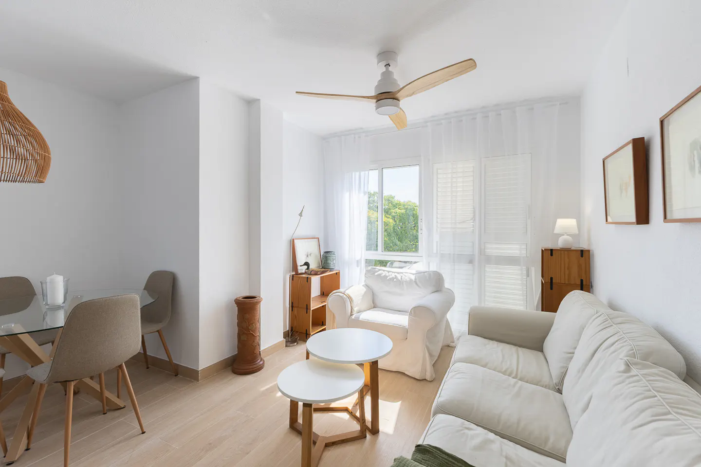 Bright living room with a white sofa, armchair, two round coffee tables, and a dining area with a glass table.