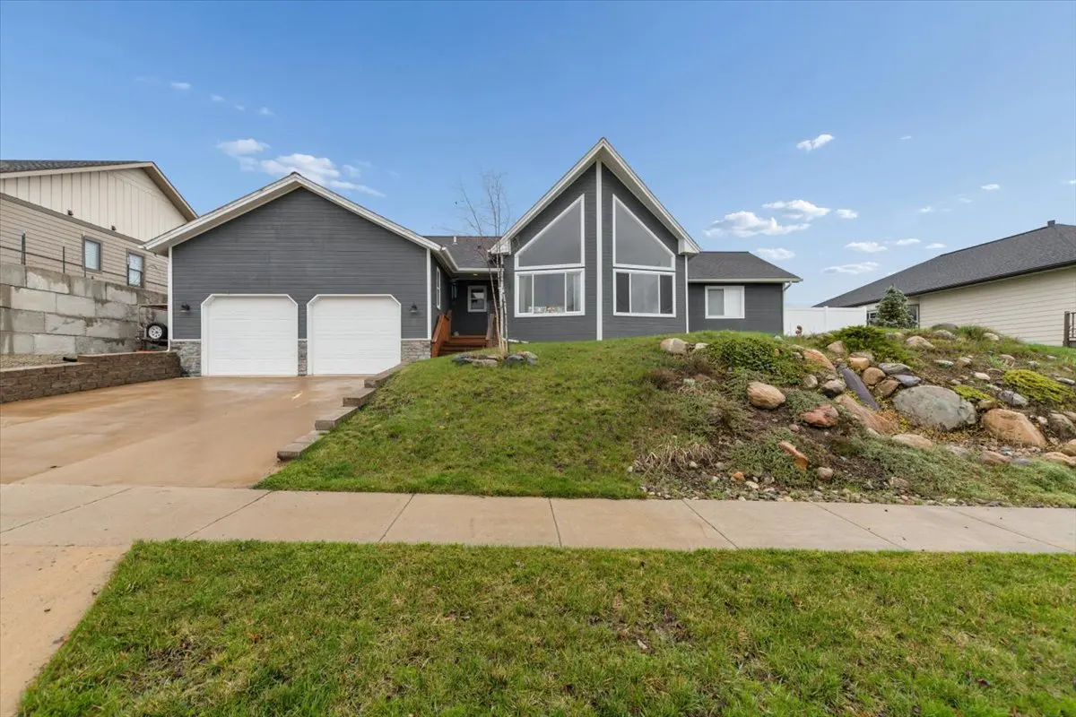 Two-story gray house with a two-car garage, green lawn, and blue sky.