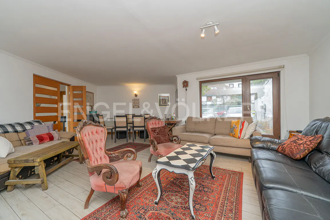Spacious living room with a black leather sofa, pink tufted armchair, beige sofa, and a checkered coffee table on a rug.