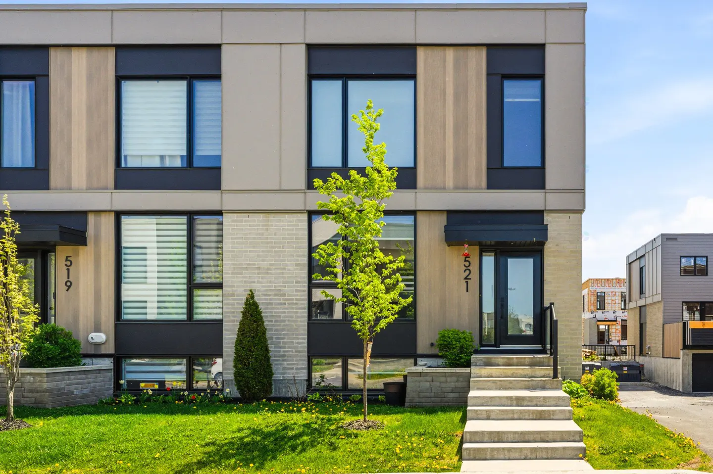 Modern townhouses with beige and gray facades, black window frames, and green lawns under a blue sky. Address numbers 519 and 521 are visible.