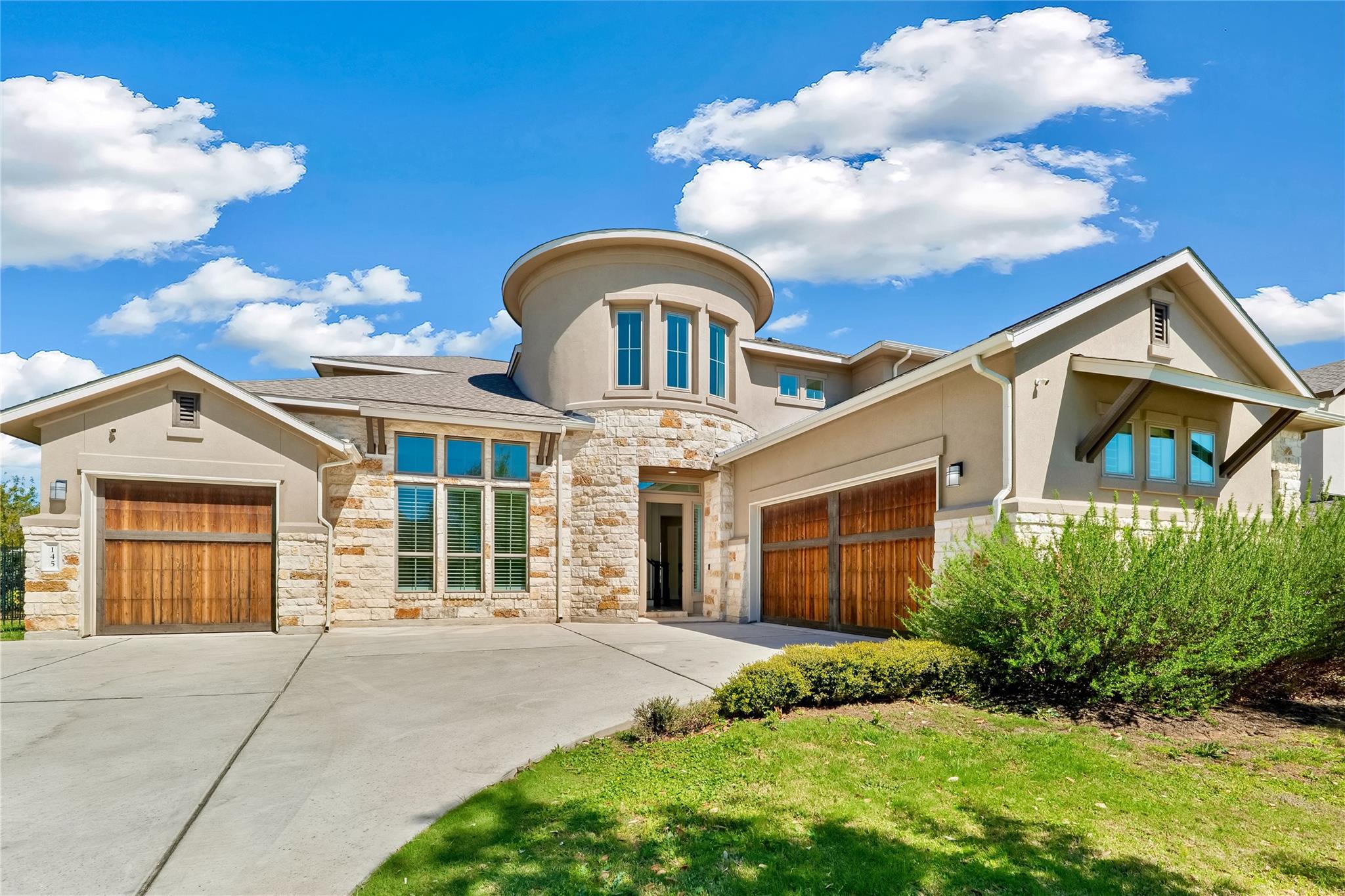 Two-story house with stone and stucco exterior, two-car garage, and a circular tower under a blue sky.