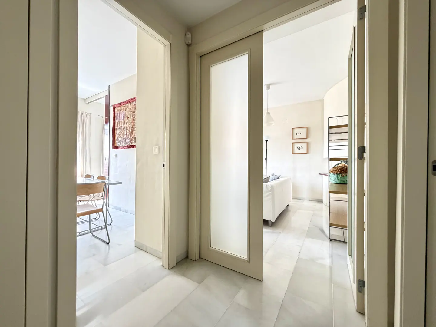 Hallway view through doorways to dining room and living room with white sofa and marble floors.