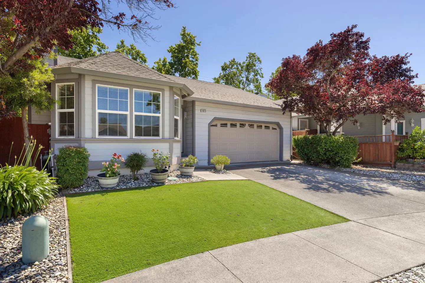 Exterior of a one-story house with gray siding, a two-car garage, and a green lawn on a sunny day.