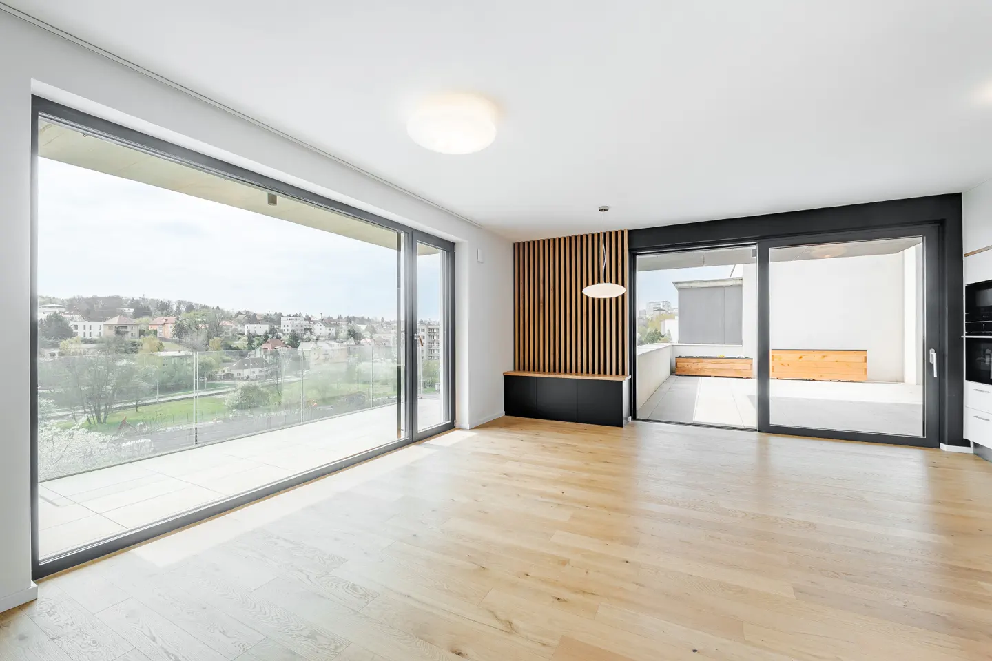 Bright, modern living room with light wood floors, large sliding glass doors to a balcony with a city view, and a wood slat accent wall.