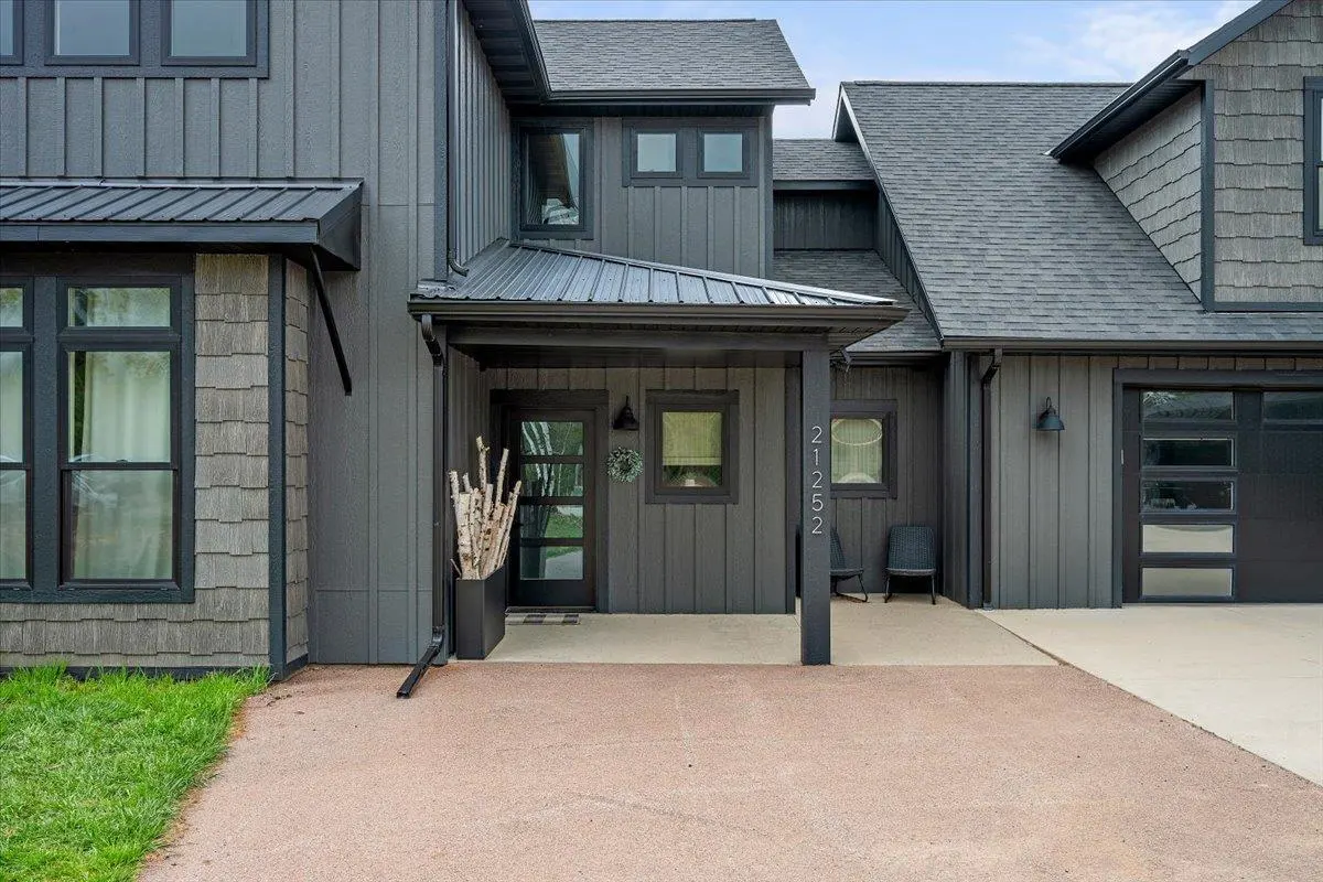 Modern gray house with black trim, a covered porch, and a garage with glass panels. A planter with birch branches sits by the front door.
