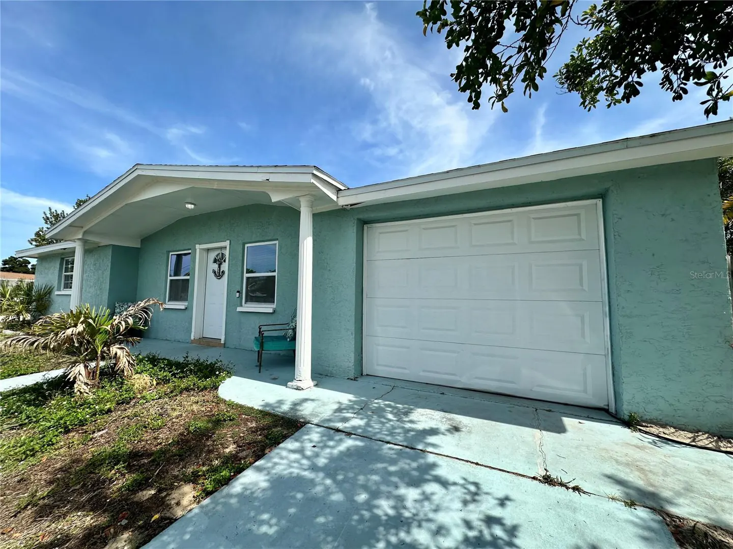 Exterior of a light blue, one-story home with a white garage door and front door with an anchor decoration.