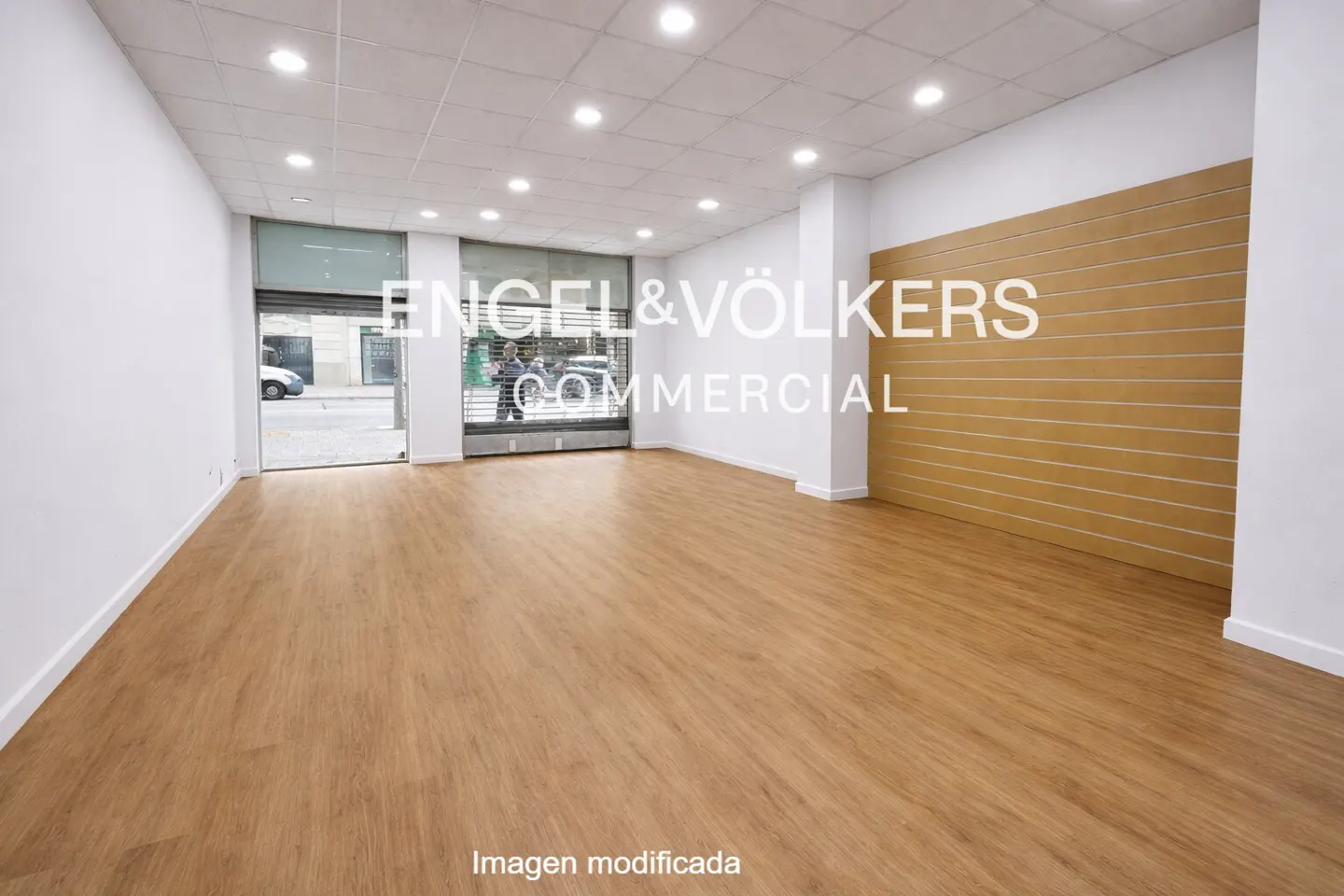 Empty commercial space with wood floors, white walls, and a large window to the street. The Engel & Völkers logo is visible on the window.