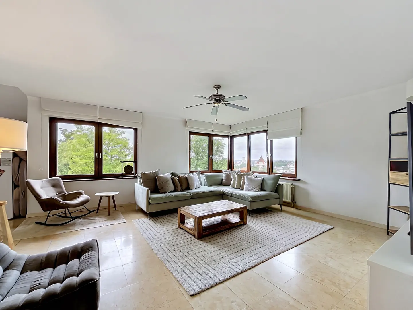 Bright living room with a sage green sectional sofa, wood coffee table, and large windows with a view.