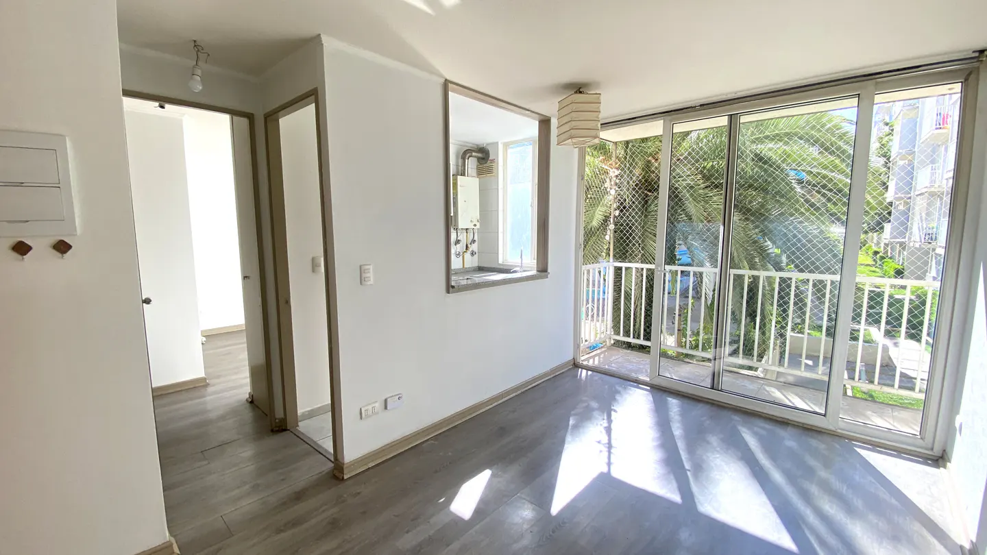 Bright, empty room with gray wood floors, white walls, and sliding glass doors to a balcony with palm tree views.