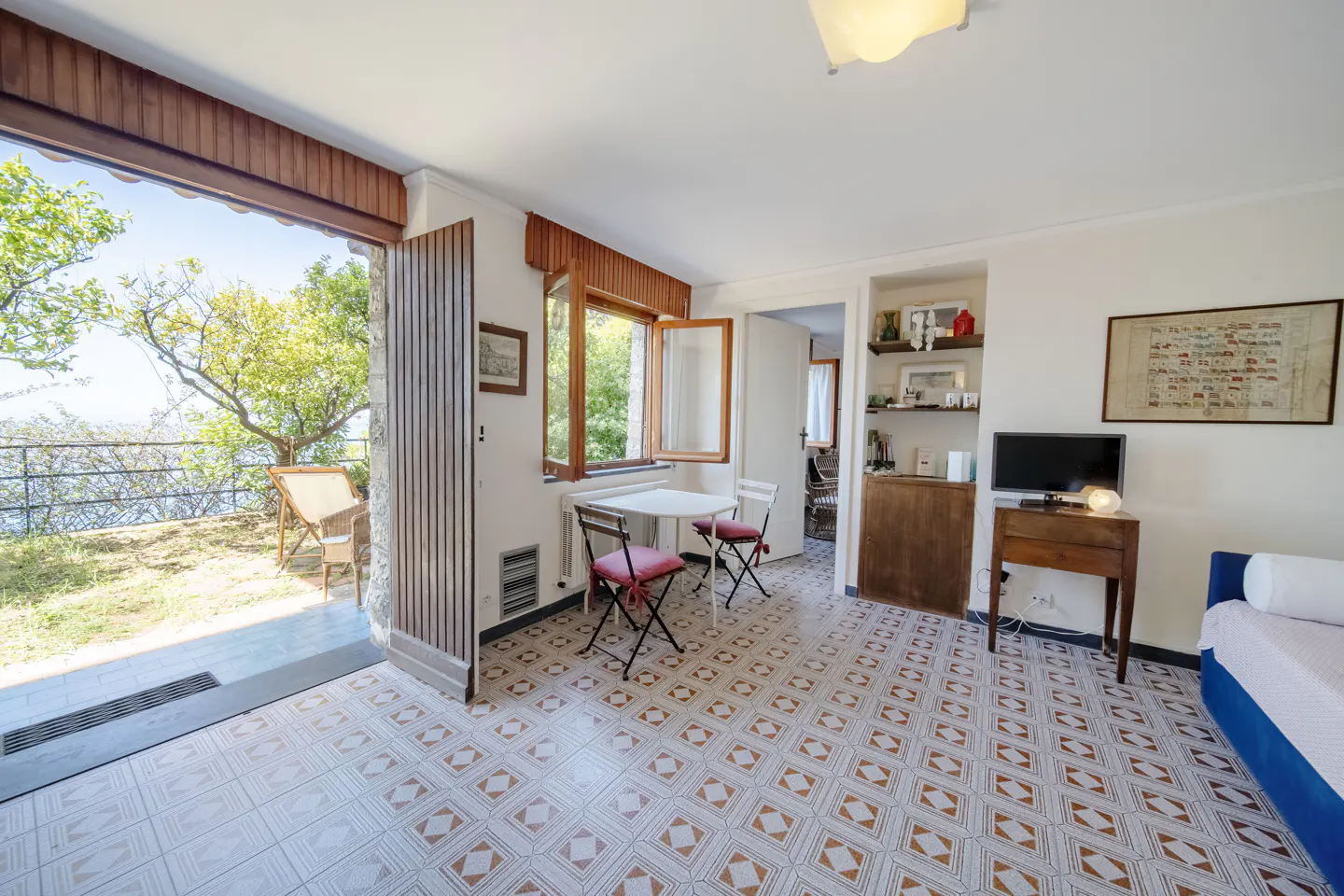 Bright living room with a small table, TV, and open patio door to a grassy area with a view of the sea.
