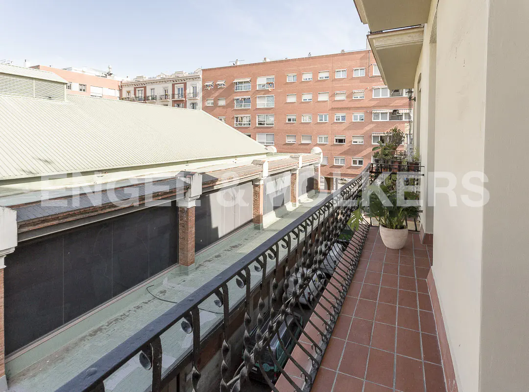 View from a balcony with black iron railings and red tile floor, overlooking a building with a white roof and a red brick apartment building.