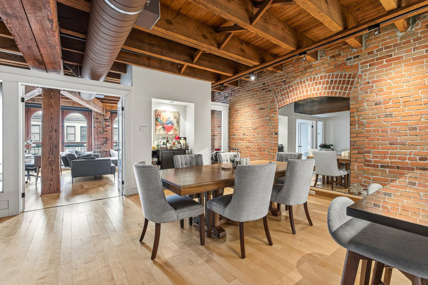 A dining room with a wooden table, gray chairs, brick walls, and exposed wooden beams.