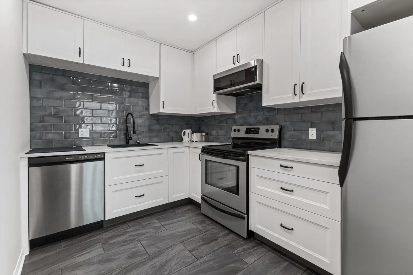 A modern kitchen with white cabinets, stainless steel appliances, and gray brick backsplash.