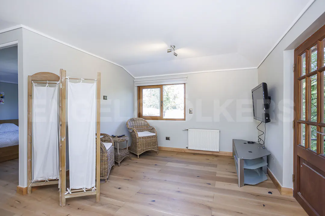 A bright living room with hardwood floors, wicker chairs, a TV, and a wooden screen.