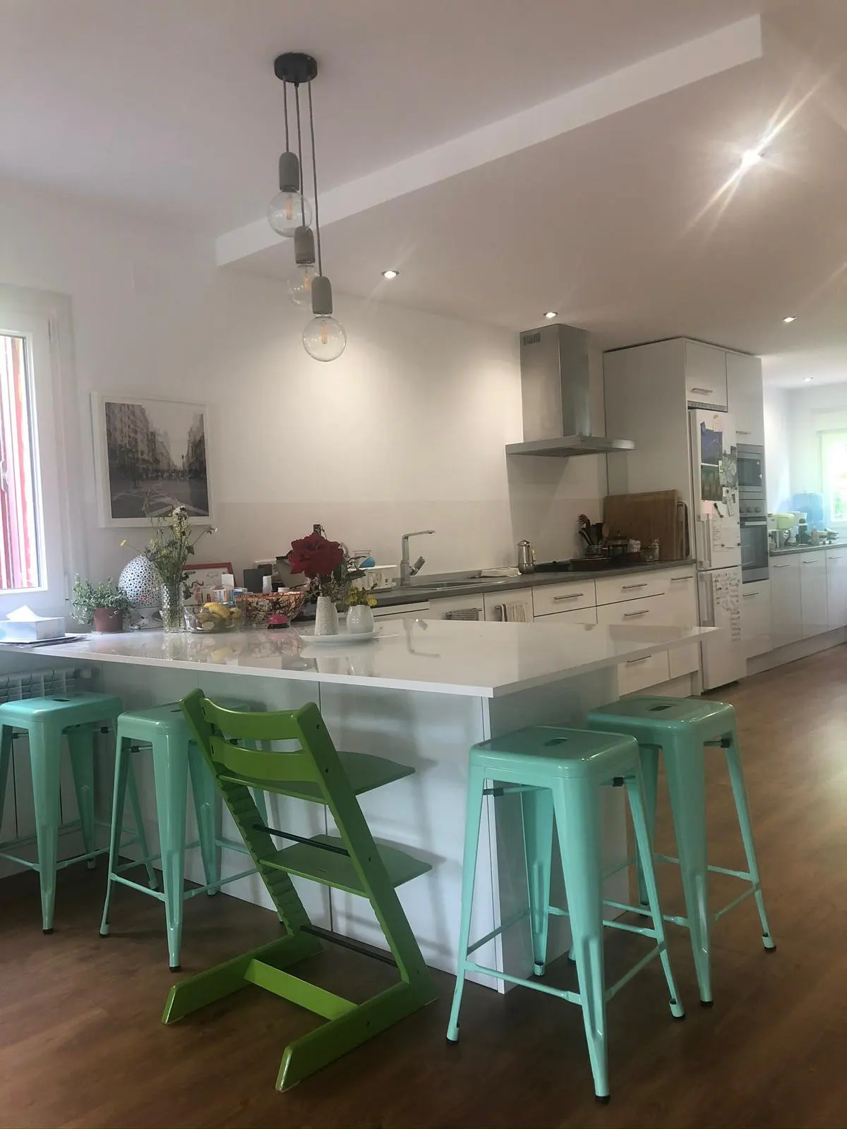 Bright, open kitchen with white cabinets, island, and mint green stools. A modern light fixture hangs above the island.