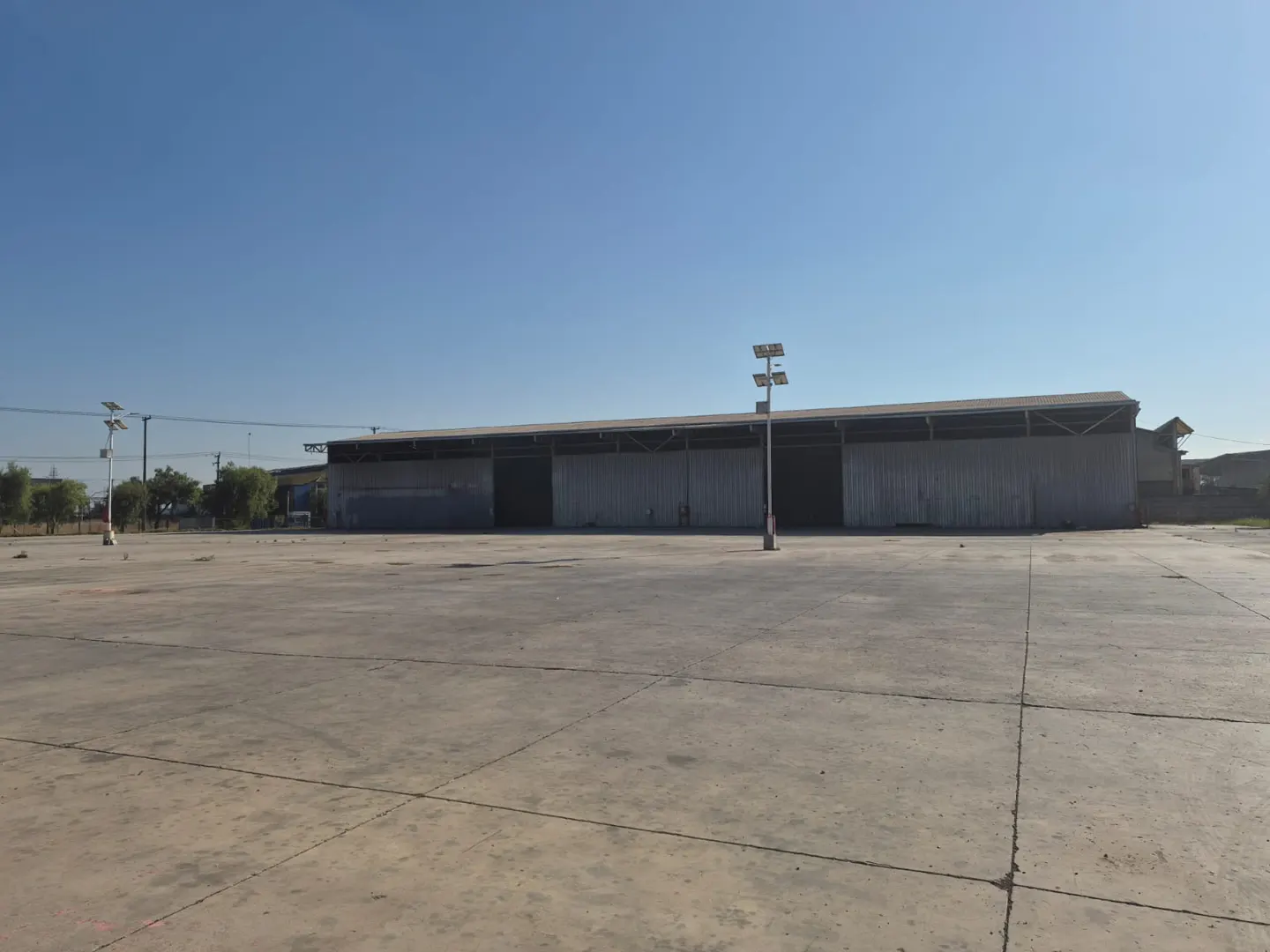 Large industrial warehouse with a vast concrete yard under a clear blue sky.