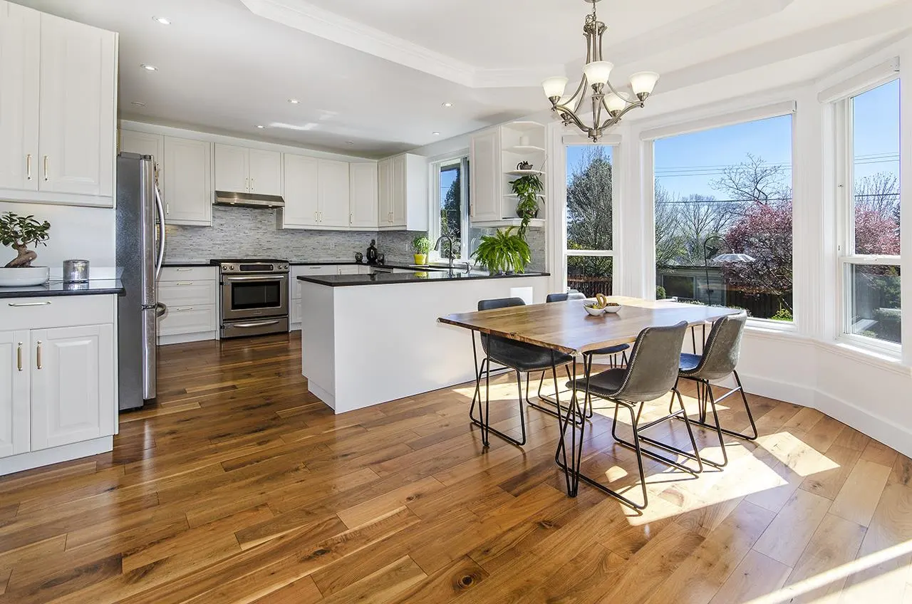 Bright kitchen with white cabinets, stainless steel appliances, and wood floors. A table and chairs sit near a bay window.
