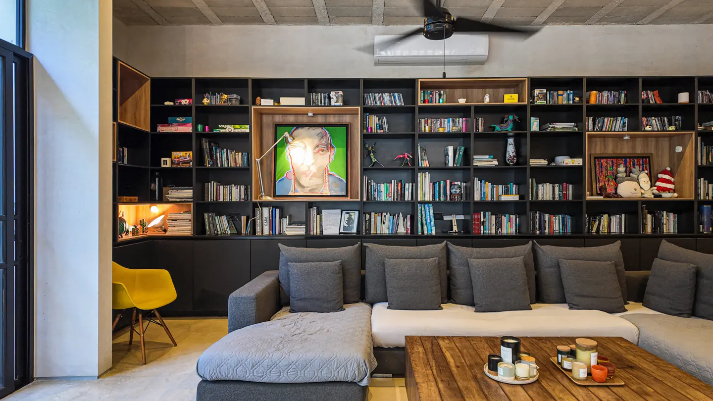 Living room with a gray sectional sofa, wooden coffee table, and a large black bookshelf filled with books and decorative items.