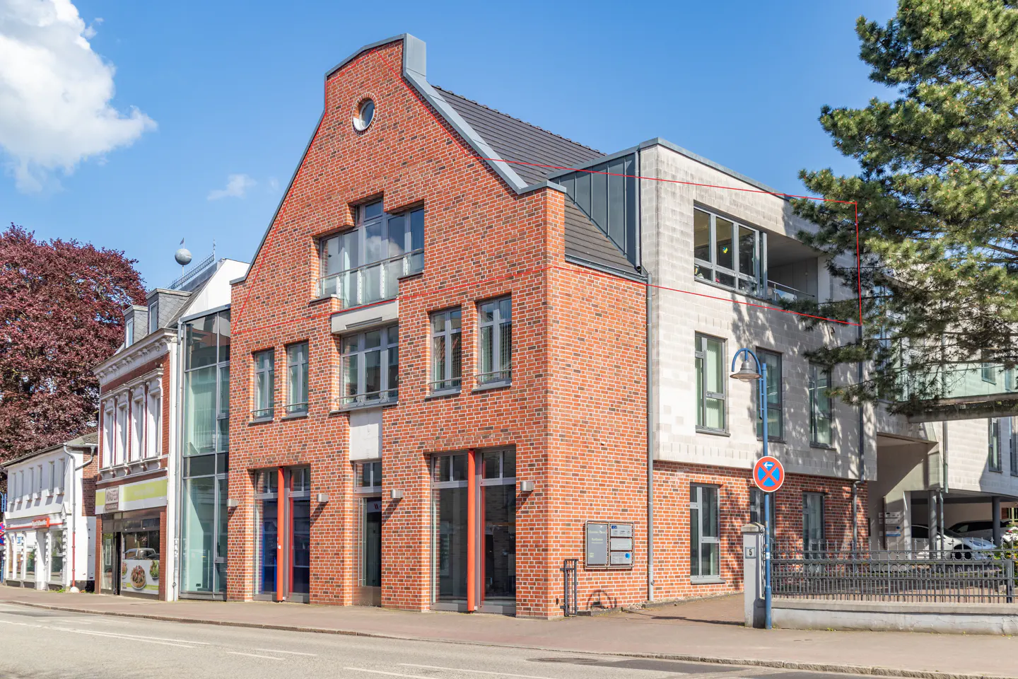 Exterior of a three-story building with red brick and gray stone facade under a blue sky.