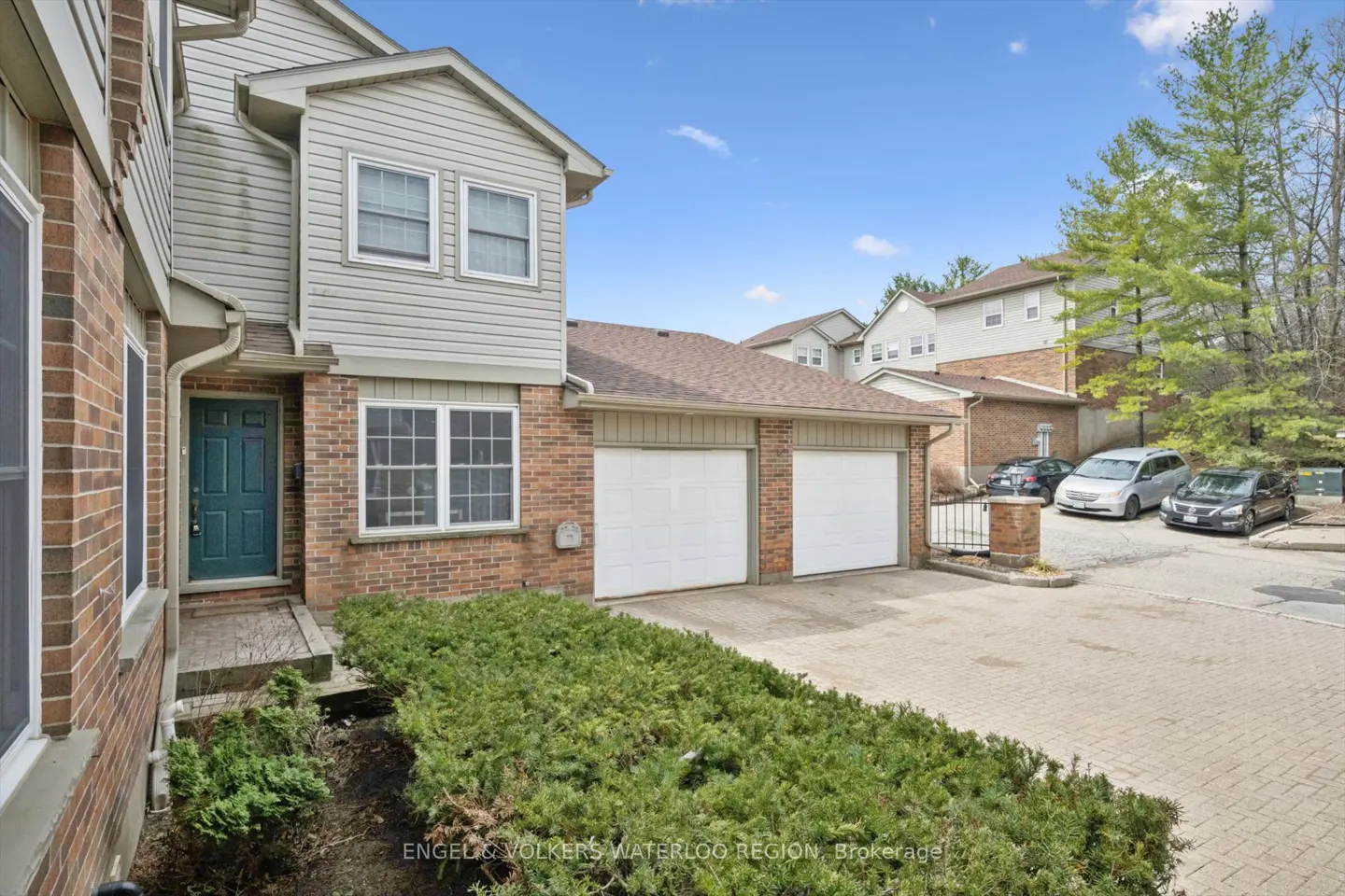 Exterior of a two-story townhouse with brick and siding, a green door, two-car garage, and green bushes.