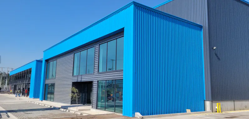 Two-story commercial building with blue and gray corrugated metal siding and large windows under a clear blue sky.