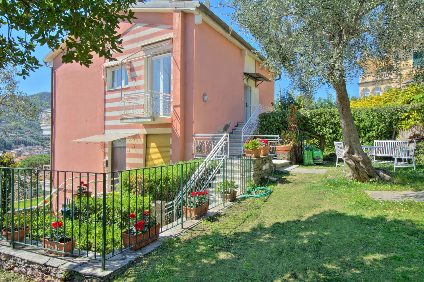 Exterior view of a two-story pink house with white trim, a green lawn, and a white bench.