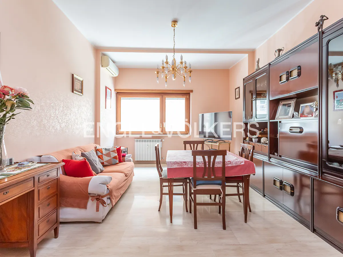 Living room with peach walls, a sofa with red pillows, a dining table with chairs, and a dark wood cabinet.