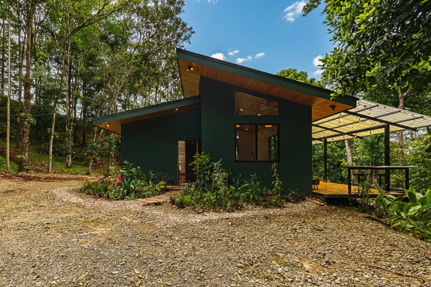 Exterior of a modern, dark green house with a wooden roof and a covered patio in a lush, green forest.