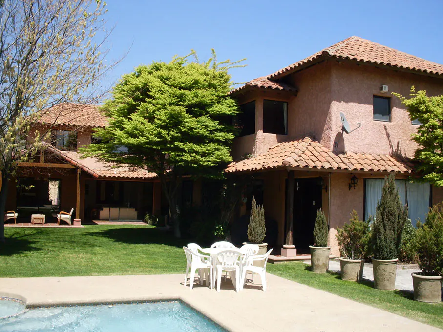 Backyard view of a terracotta-roofed house with a pool, green lawn, and white patio furniture.