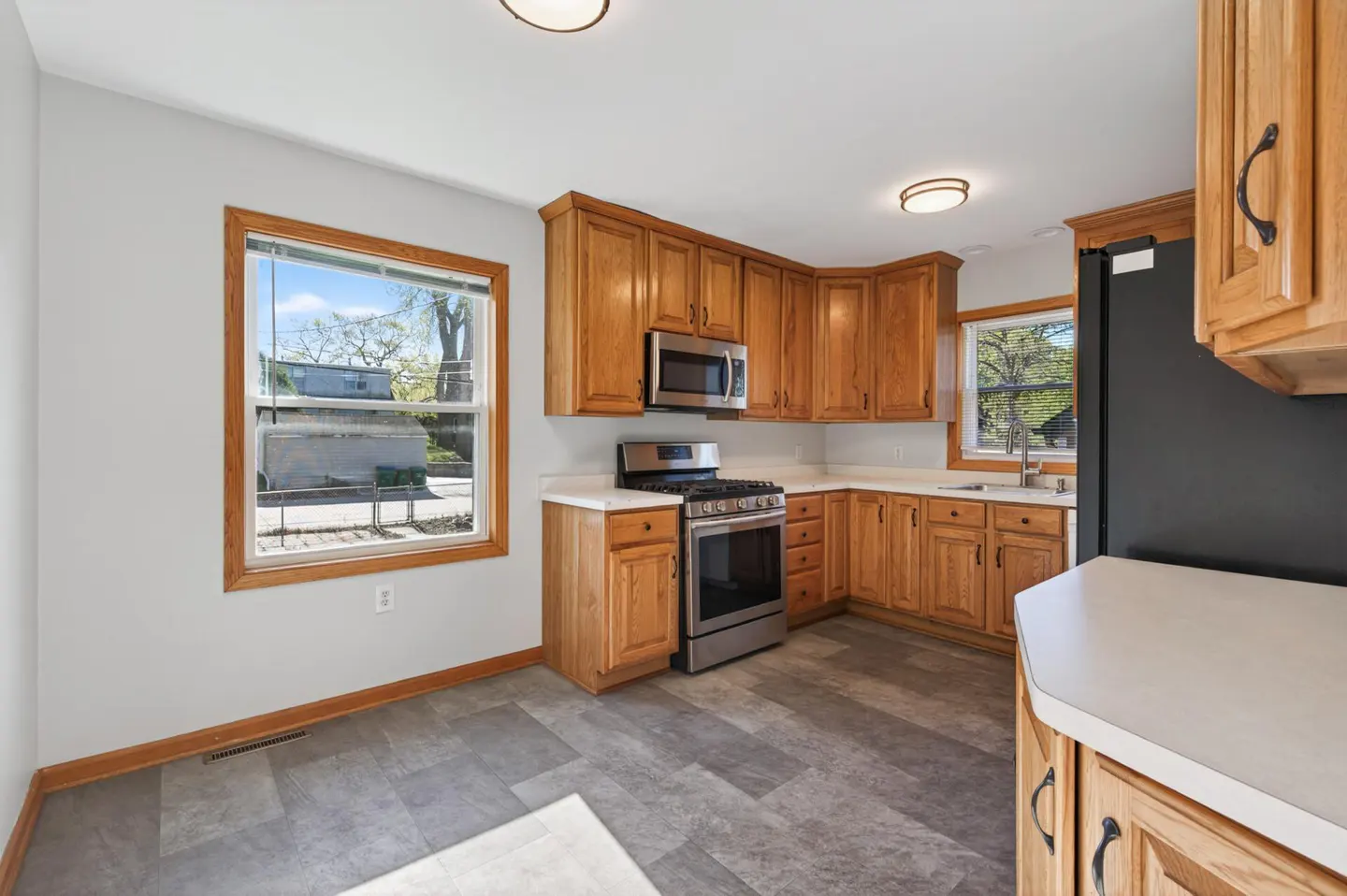 Bright kitchen with gray floors, oak cabinets, and white countertops. Stainless steel appliances include a microwave and gas range. A window overlooks the yard.