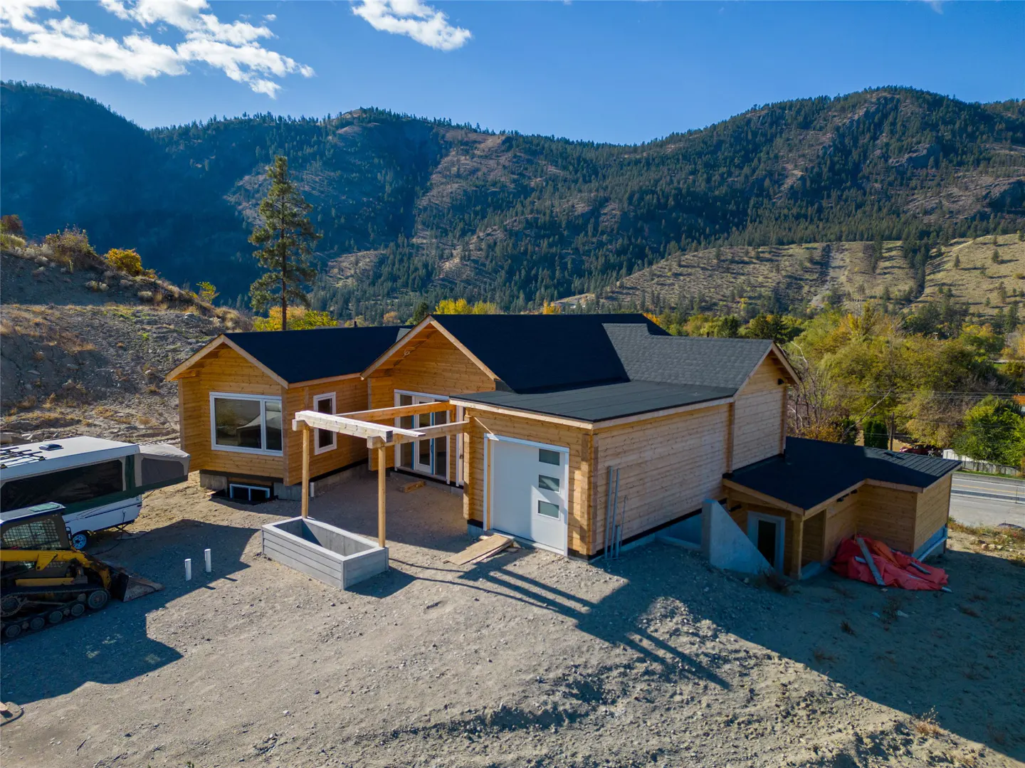 Aerial view of a light wood home with a black roof, a garage, and a mountain backdrop.