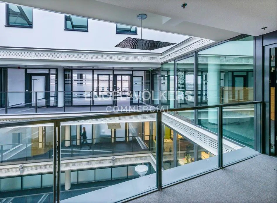 Interior view of a modern commercial building with glass railings and open atrium. White walls, black window frames, and a person walking in the background.